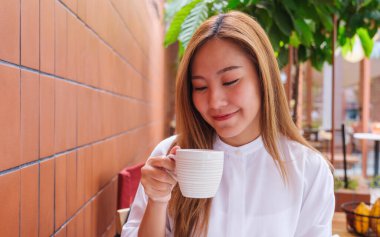 Asyalı güzel bir kadının portre resmi. Sıcak kahve tutuyor ve içiyor.