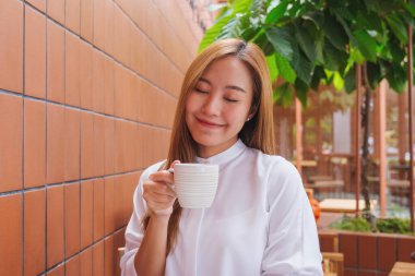 Asyalı güzel bir kadının portre resmi. Sıcak kahve tutuyor ve içiyor.