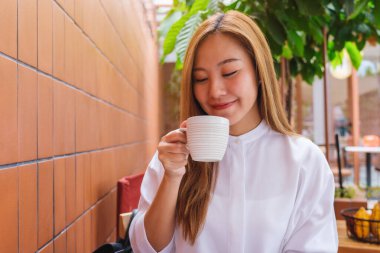 Asyalı güzel bir kadının portre resmi. Sıcak kahve tutuyor ve içiyor.
