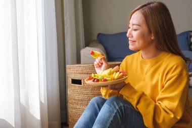 Şişler üzerinde taze karışık meyveler tutan ve yiyen genç bir kadının portresi.