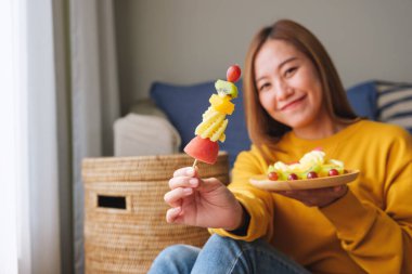 Şişler üzerinde taze karışık meyveler tutan ve yiyen genç bir kadının portresi.