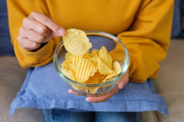 Evde patates cipsi toplayıp yiyen bir kadının yakın plan fotoğrafı.