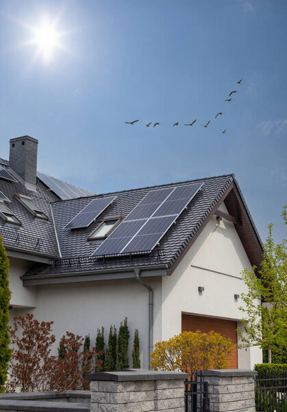 Solar Panel on a dark gable roof - blue sky and sun. Moder house, vertical shot.