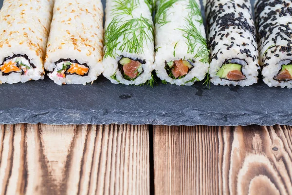 Rolos de sushi uramaki caseiros em um quadro de ardósia — Fotografia de Stock