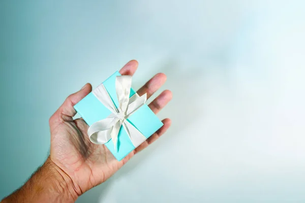 Mano sosteniendo una caja de regalo de turquesa atada con cinta de seda blanca — Foto de Stock