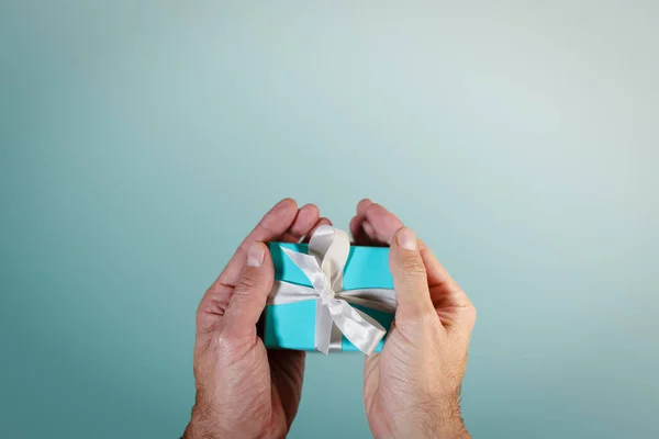 Handen met een turquoise geschenkdoos gebonden met wit satijnen lint Rechtenvrije Stockfoto's