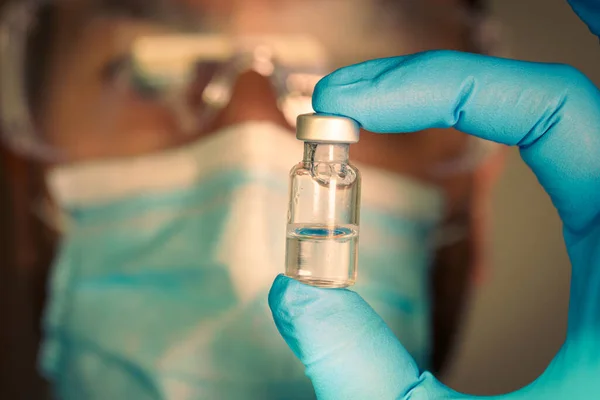 Detailní záběr injekční lahvičky s rozmazaným lékařem na pozadí. — Stock fotografie
