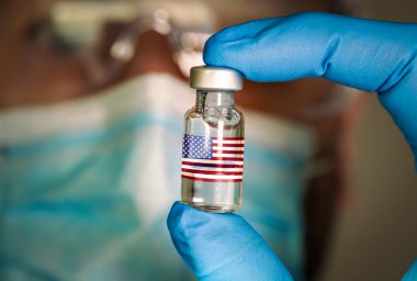 Arka planda bulanık doktor ve Amerikan bayrağı olan tıbbi şişenin yakın plan görüntüsü..