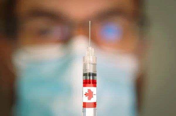 Close-up of hypodermic syringe with the canadian flag and blurred doctor on the background. — Stock Photo, Image