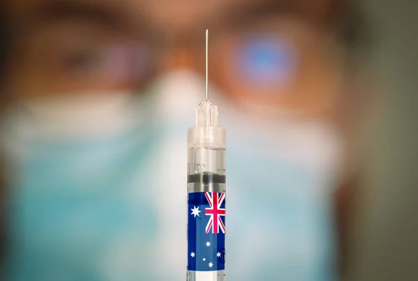 Close-up of hypodermic syringe with the Australian flag and blurred doctor on the background. — Stock Photo, Image