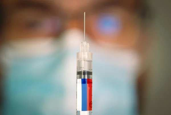 Close-up of hypodermic syringe with the russian flag and blurred doctor on the background. — Stock Photo, Image