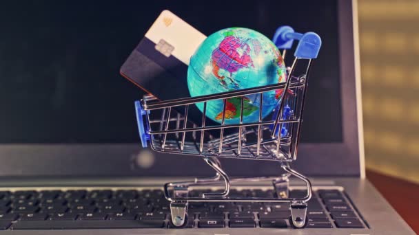 Pequeño carrito de compras con mundo globo en él sobre un ordenador portátil. — Vídeos de Stock