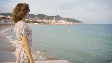 Güzel kıvırcık esmer turist Akdeniz köyü Sitges 'e bakıyor.