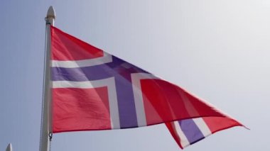 Norveç bayrağı yavaş çekimde mavi gökyüzünde dalgalanıyor