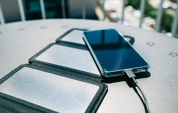 Carregando um smartphone de casa com um carregador de painel solar portátil. Auto-consumo e carregamento com pequenos painéis solares i — Fotografia de Stock