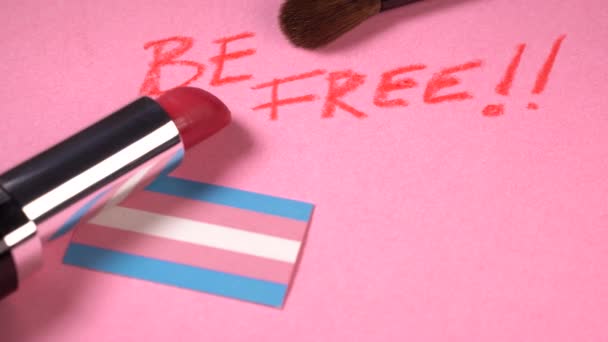 Be free expression with lipstick and make-up brushes close up view over a transgender flag — Stock Video