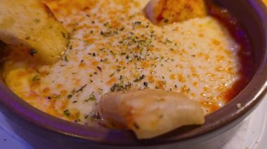 Hot and bubbling baked provolone cheese, also known as provoleta, served in a traditional earthenware dish with tomato sauce, sprinkled with oregano, and accompanied by bread for dipping