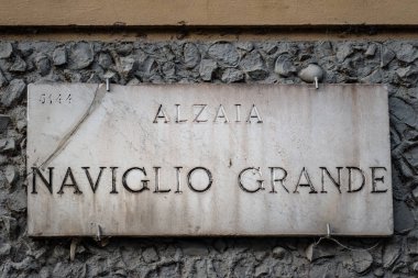Milan, İtalya. 6 Aralık 2025, Marble Caddesi imzalı Alzaia Naviglio Grande Milans tarihi kanal bölgesini gösteren yıpranmış taş duvar, kentsel detayları kapatın.