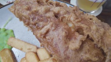 Klasik bir tabak İngiliz balık ve patates kızartması, kızarmış balık, kalın kesilmiş patates kızartması, lapa ve tartar sosu bir restoranda servis edilen rustik bir tabakta.