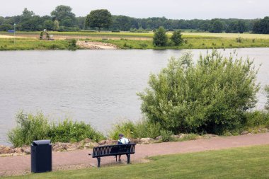 Woman reading book at bench near Dutch river Meuse