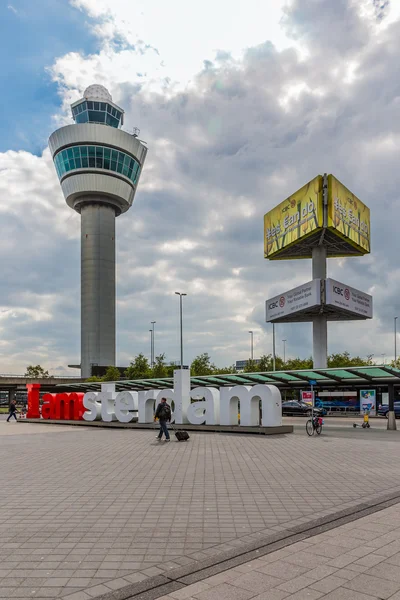 Luchthaven plein met verkeerstoren, reclame pijler en passerende reizigers — Stockfoto