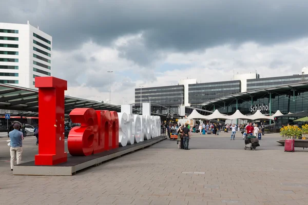 Luchthaven plein met amsterdam logo en onbekende reizigers — Stockfoto