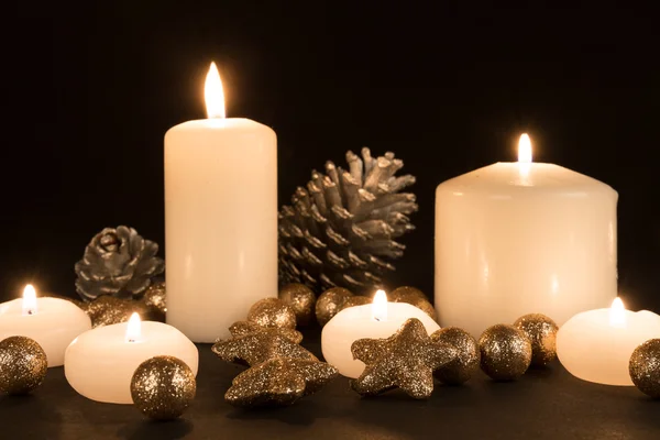 Candele ardenti con mele di pino e stelle dorate su sfondo nero — Foto Stock