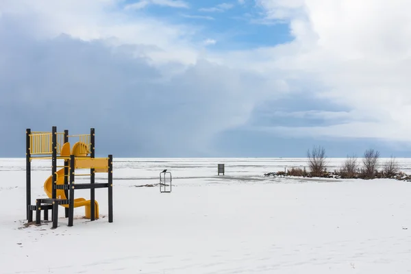 Playa nevada cerca de un mar congelado con un parque infantil — Foto de Stock