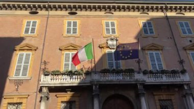 Hükümet binasının balkonunda rüzgarda sallanan İtalyan ve Avrupa bayrakları. Turizm, vatanseverlik, uluslararası ticaret, politika, ticaret konsepti