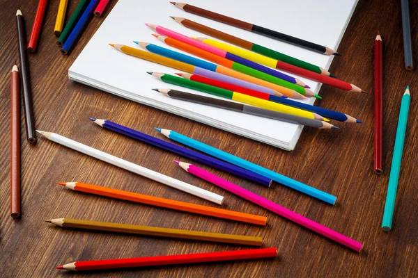 Kleurrijke potloden op houten tafel met papier. Bovenaanzicht — Stockfoto