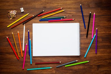 Boş kağıt ve ahşap masada renkli kalemler. Üst görünüm