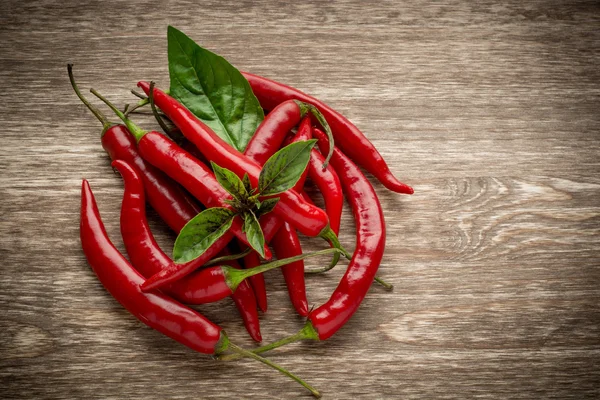 Red hot chili peppers en basilicum bladeren op houten achtergrond. kopie ruimte, leeg bord — Stockfoto