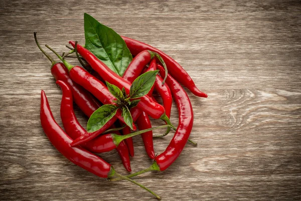 Chiles rojos picantes y hojas de albahaca sobre fondo de madera. Copiar espacio, tablero en blanco — Foto de Stock