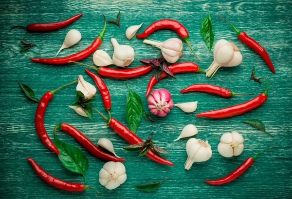 Rode chilipepertjes, knoflook en basilicum op een houten achtergrond — Stockfoto