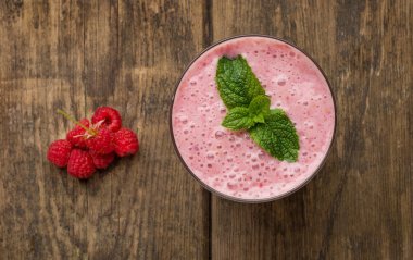 Raspberry smoothie in a glass on wooden table, top view