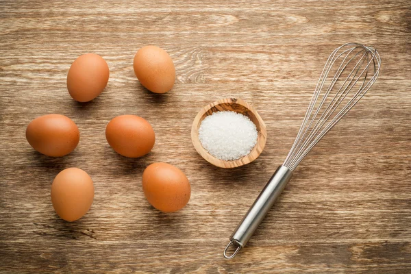 Eggs with beater and salt on wooden table — Stock Photo, Image