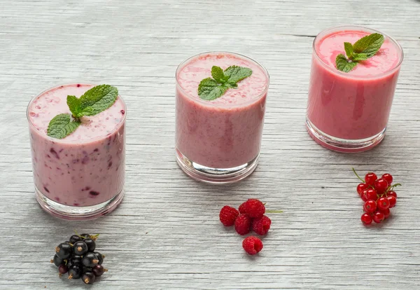 Leche fresca, grosella, frambuesa y rojo grosella bebidas en la mesa de wodeen, surtido de cócteles de proteínas con frutas frescas —  Fotos de Stock