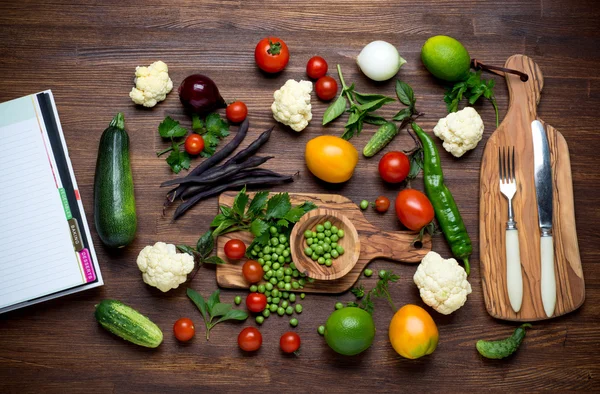 Gezonde voeding. Kruiden en groenten op houten tafel met receptenboek. Bovenaanzicht. — Stockfoto
