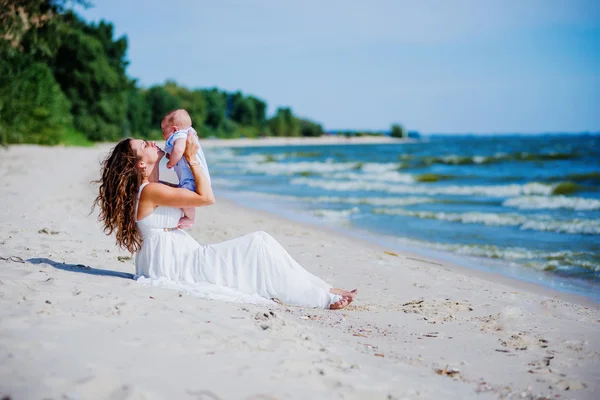 Счастливая семья. Молодая мать бросает ребенка в небо, в солнечный день на пляже . — стоковое фото