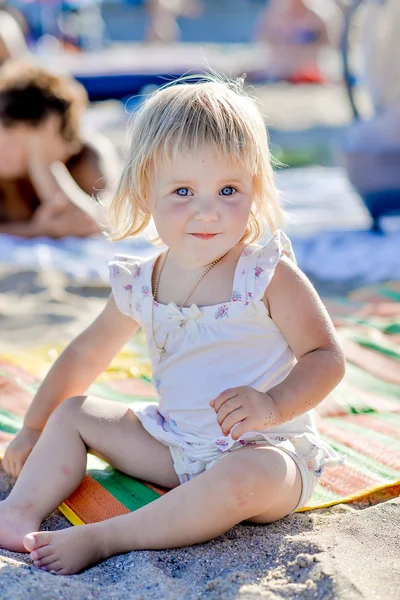 Küçük bir kız gülümser ve kum plajında oturur — Stok fotoğraf