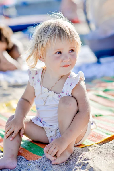 Küçük bir kız gülümser ve kum plajında oturur — Stok fotoğraf