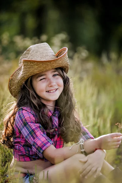 Niña sentada en un campo con un sombrero de vaquero — Foto de Stock