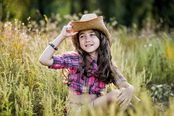 Malá dívka sedící v poli kovbojský klobouk — Stock fotografie