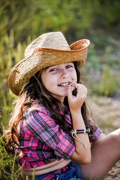 Menina sentada em um campo usando um chapéu de cowboy — Fotografia de Stock