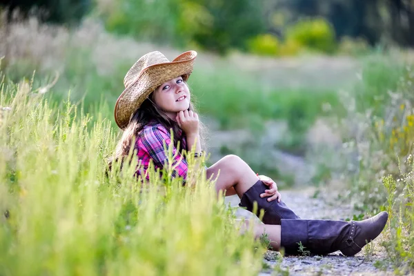 Niña sentada en un campo con un sombrero de vaquero — Foto de Stock