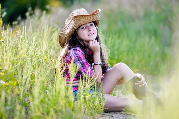 Niña sentada en un campo con un sombrero de vaquero — Foto de Stock