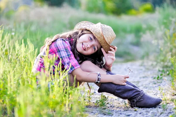 Niña sentada en un campo con un sombrero de vaquero — Foto de Stock