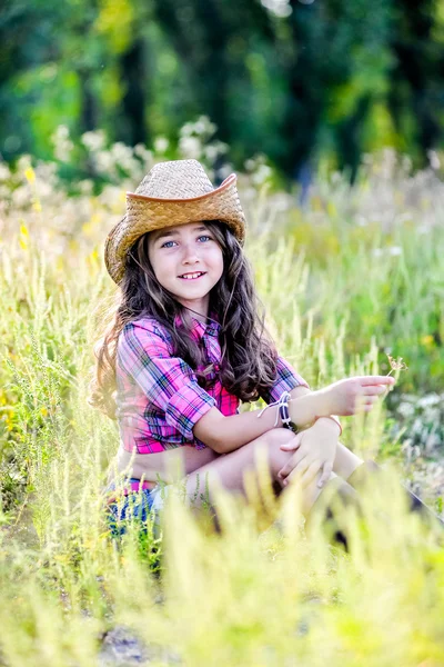 Meisje zittend in een veld met een cowboy hoed — Stockfoto