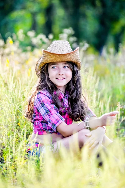 Meisje zittend in een veld met een cowboy hoed — Stockfoto