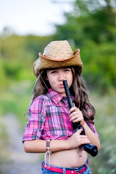 Niña con una pistola de juguete en la mano de pie en un campo — Foto de Stock